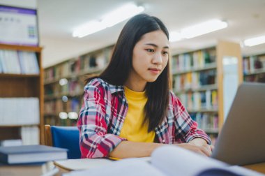 Dizüstü bilgisayarda çalışan ve okuyacak kitaplar arayan, rapor hazırlayan, üniversite odasında işe yarar bilgiler bulan bir üniversite öğrencisi. Okuma, öğrenme ve zeka kavramı.