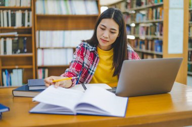 Dizüstü bilgisayarda çalışan ve okuyacak kitaplar arayan, rapor hazırlayan, üniversite odasında işe yarar bilgiler bulan bir üniversite öğrencisi. Okuma, öğrenme ve zeka kavramı.