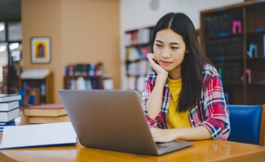 Dizüstü bilgisayarda çalışan ve okuyacak kitaplar arayan, rapor hazırlayan, üniversite odasında işe yarar bilgiler bulan bir üniversite öğrencisi. Okuma, öğrenme ve zeka kavramı.