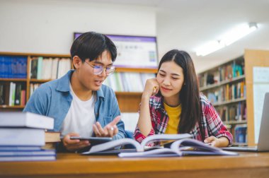 Öğrenciler birbirlerine danışarak dizüstü bilgisayarlar üzerinde çalışıyor ve çalışmak için kitaplar arıyor, raporlar hazırlıyor, üniversite odasında yararlı bilgiler buluyor. Okuma, öğrenme ve zeka kavramı.