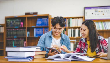 Öğrenciler birbirlerine danışarak dizüstü bilgisayarlar üzerinde çalışıyor ve çalışmak için kitaplar arıyor, raporlar hazırlıyor, üniversite odasında yararlı bilgiler buluyor. Okuma, öğrenme ve zeka kavramı.