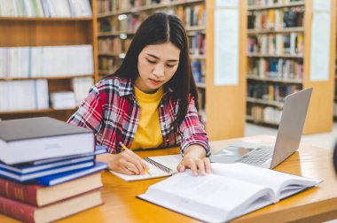 Dizüstü bilgisayarda çalışan ve okuyacak kitaplar arayan, rapor hazırlayan, üniversite odasında işe yarar bilgiler bulan bir üniversite öğrencisi. Okuma, öğrenme ve zeka kavramı.