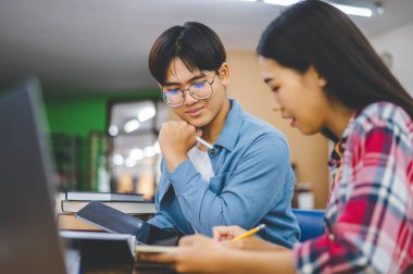 Öğrenciler birbirlerine danışarak dizüstü bilgisayarlar üzerinde çalışıyor ve çalışmak için kitaplar arıyor, raporlar hazırlıyor, üniversite odasında yararlı bilgiler buluyor. Okuma, öğrenme ve zeka kavramı.