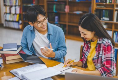 Öğrenciler birbirlerine danışarak dizüstü bilgisayarlar üzerinde çalışıyor ve çalışmak için kitaplar arıyor, raporlar hazırlıyor, üniversite odasında yararlı bilgiler buluyor. Okuma, öğrenme ve zeka kavramı.