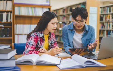 Öğrenciler birbirlerine danışarak dizüstü bilgisayarlar üzerinde çalışıyor ve çalışmak için kitaplar arıyor, raporlar hazırlıyor, üniversite odasında yararlı bilgiler buluyor. Okuma, öğrenme ve zeka kavramı.