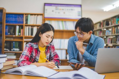 Öğrenciler birbirlerine danışarak dizüstü bilgisayarlar üzerinde çalışıyor ve çalışmak için kitaplar arıyor, raporlar hazırlıyor, üniversite odasında yararlı bilgiler buluyor. Okuma, öğrenme ve zeka kavramı.