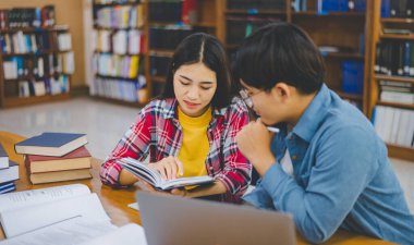 Öğrenciler birbirlerine danışarak dizüstü bilgisayarlar üzerinde çalışıyor ve çalışmak için kitaplar arıyor, raporlar hazırlıyor, üniversite odasında yararlı bilgiler buluyor. Okuma, öğrenme ve zeka kavramı.