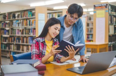 Öğrenciler birbirlerine danışarak dizüstü bilgisayarlar üzerinde çalışıyor ve çalışmak için kitaplar arıyor, raporlar hazırlıyor, üniversite odasında yararlı bilgiler buluyor. Okuma, öğrenme ve zeka kavramı.