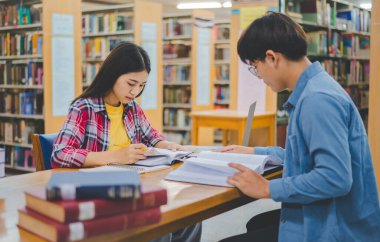 Öğrenciler birbirlerine danışarak dizüstü bilgisayarlar üzerinde çalışıyor ve çalışmak için kitaplar arıyor, raporlar hazırlıyor, üniversite odasında yararlı bilgiler buluyor. Okuma, öğrenme ve zeka kavramı.