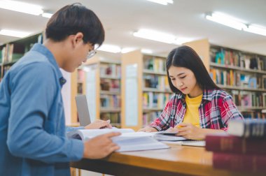 Öğrenciler birbirlerine danışarak dizüstü bilgisayarlar üzerinde çalışıyor ve çalışmak için kitaplar arıyor, raporlar hazırlıyor, üniversite odasında yararlı bilgiler buluyor. Okuma, öğrenme ve zeka kavramı.
