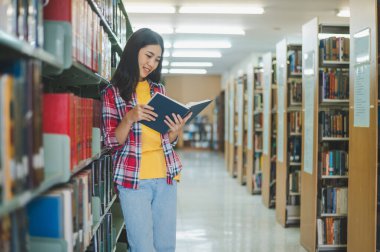 Öğrenciler okumak ve okumak için kitap arıyorlar, rapor hazırlıyorlar, kütüphanedeki kitaplıklarda yararlı bilgiler buluyorlar. Okuma, öğrenme ve zeka kavramı.