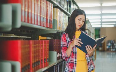 Öğrenciler okumak ve okumak için kitap arıyorlar, rapor hazırlıyorlar, kütüphanedeki kitaplıklarda yararlı bilgiler buluyorlar. Okuma, öğrenme ve zeka kavramı.