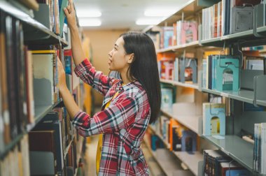 Okumak için kitap arayan, rapor hazırlayan, kütüphanedeki kitaplıklarda yararlı bilgiler bulan kız üniversite öğrencileri. Okuma, öğrenme ve zeka kavramı.