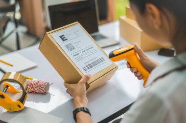 Çevrimiçi küçük işletme sahibi, müşteriye teslim edilmeden önce müşterinin siparişini doğrulamak için barkod tarayıcı ile etiketli bir paket tarar.
