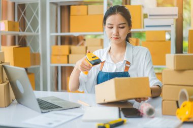 Çevrimiçi küçük işletme sahibi, müşteriye teslim edilmeden önce müşterinin siparişini doğrulamak için barkod tarayıcı ile etiketli bir paket tarar.