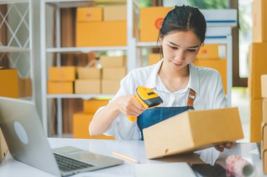 Çevrimiçi küçük işletme sahibi, müşteriye teslim edilmeden önce müşterinin siparişini doğrulamak için barkod tarayıcı ile etiketli bir paket tarar.