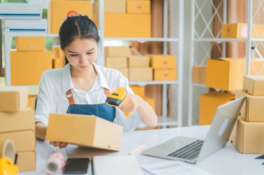 Çevrimiçi küçük işletme sahibi, müşteriye teslim edilmeden önce müşterinin siparişini doğrulamak için barkod tarayıcı ile etiketli bir paket tarar.