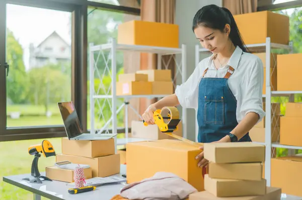 Startup small business owners holding packing machine and sealing cardboard boxes with tape to deliver products to customers- concept shopping online