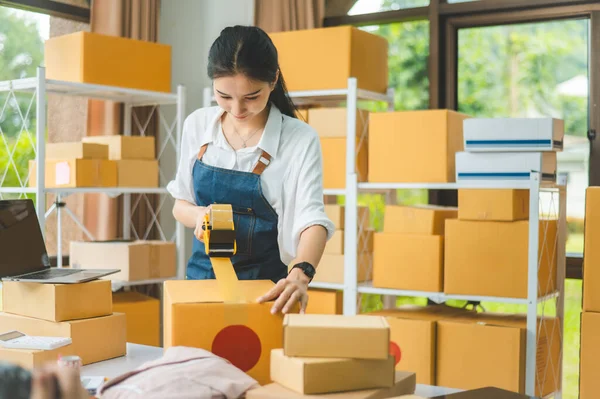 Startup small business owners holding packing machine and sealing cardboard boxes with tape to deliver products to customers- concept shopping online