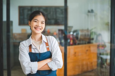 Gülümseyen Asyalı kahve dükkanı sahibi kasiyerin önünde duruyor. Kafeye sipariş vermek için gelen müşterileri hoş karşılar..