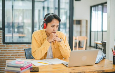 Genç Asyalı üniversite öğrencisi kafede dizüstü bilgisayarda çalışıyor ve öğreniyor. İnternette bilgi aranıyor.