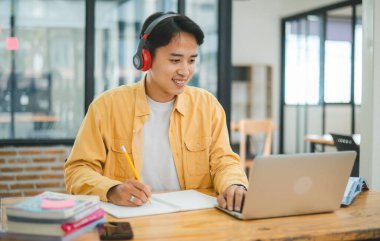Genç Asyalı üniversite öğrencisi kafede dizüstü bilgisayarda çalışıyor ve öğreniyor. İnternette bilgi aranıyor.