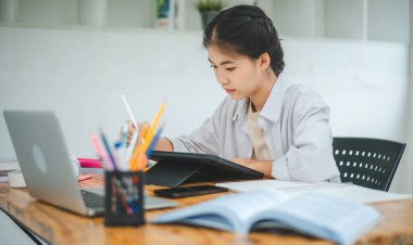 Genç Asyalı üniversite öğrencisi rapor hazırlıyor, kafede tablet çiziyor. İnternette iletişim ve araştırma.