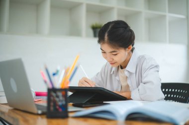 Genç Asyalı üniversite öğrencisi rapor hazırlıyor, kafede tablet çiziyor. İnternette iletişim ve araştırma.