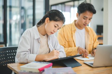 Ödev yapan genç üniversite öğrencileri, işbirliği yapan araştırma planı kavramları ve stratejileri tartışıyor. Dizüstü bilgisayarlarda ve tablet bilgisayarlarda sunumları hazırlayın.