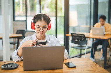 Öğrenci, bir kafede kulaklık takarken dizüstü bilgisayar kullanıyor, internette öğreniyor ve arama yapıyor..