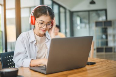Öğrenci, bir kafede kulaklık takarken dizüstü bilgisayar kullanıyor, internette öğreniyor ve arama yapıyor..