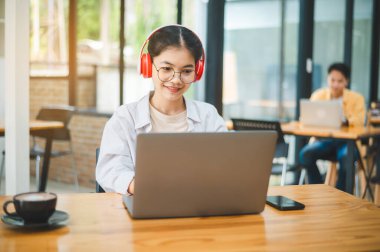 Öğrenci, bir kafede kulaklık takarken dizüstü bilgisayar kullanıyor, internette öğreniyor ve arama yapıyor..