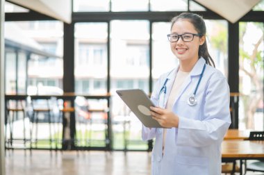 Steteskoplu ve dijital tablet kullanan portre doktoru hastane veya klinikteki sağlık hizmetleri ziyaretçilerine güvenle hazırdır..