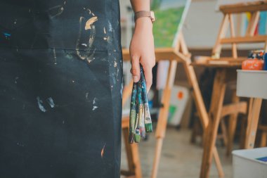 Resim öğrencisinin elinde boya fırçasıyla tuvaldeki suluboya resme bazı sanat projeleri yapıyor.