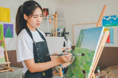 Resim öğrencisi tuvale suluboya resim çiziyor. Stüdyo atölyesinde bazı sanat projeleri yapıyor.