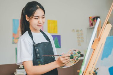 Resim öğrencisi tuvale suluboya resim çiziyor. Stüdyo atölyesinde bazı sanat projeleri yapıyor.