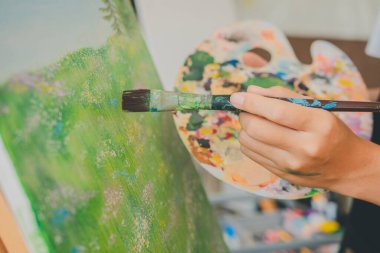 Stüdyo atölyesinde bazı sanat projeleri yapmak için suluboya boya fırça kullanarak resim öğrencisinin elini kapatıyoruz.