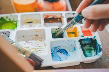 Tablo üzerindeki suluboya resme başlamadan önce resim yapmak için boya fırçası ve suluboya boya boya kullanmanın yakın çekimi.