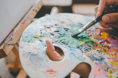Resim öğrencisinin elini boya fırçasıyla boyayarak bir paletin rengini, resim projeleri yaparken suluboya resimlerle karıştırıyor.