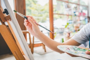 Stüdyo atölyesinde bazı sanat projeleri yapmak için suluboya boya fırça kullanarak resim öğrencisinin elini kapatıyoruz.