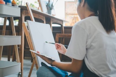 Resim öğrencisi tuvale suluboya resim çiziyor. Stüdyo atölyesinde bazı sanat projeleri yapıyor.