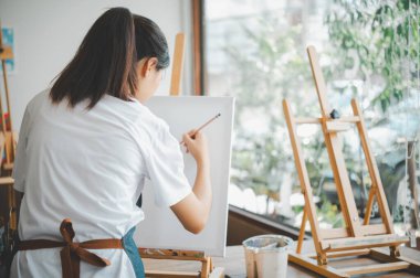 Resim öğrencisi tuvale suluboya resim çiziyor. Stüdyo atölyesinde bazı sanat projeleri yapıyor.