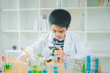 Asyalı erkek bilim öğrencileri mikroskopla bakıyorlar ve sınıfta bitki testleri yapıyorlar. Bitki türleri üzerinde bilimsel deneyler öğrenmek.