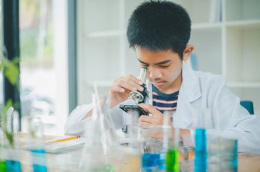 Asyalı erkek bilim öğrencileri mikroskopla bakıyorlar ve sınıfta bitki testleri yapıyorlar. Bitki türleri üzerinde bilimsel deneyler öğrenmek.