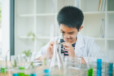 Asyalı erkek bilim öğrencileri mikroskopla bakıyorlar ve sınıfta bitki testleri yapıyorlar. Bitki türleri üzerinde bilimsel deneyler öğrenmek.