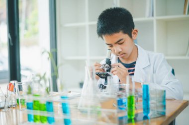 Asyalı erkek bilim öğrencileri mikroskopla bakıyorlar ve sınıfta bitki testleri yapıyorlar. Bitki türleri üzerinde bilimsel deneyler öğrenmek.