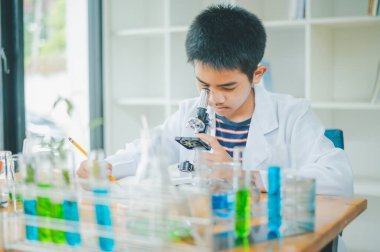 Asyalı erkek bilim öğrencileri mikroskopla bakıyorlar ve sınıfta bitki testleri yapıyorlar. Bitki türleri üzerinde bilimsel deneyler öğrenmek.