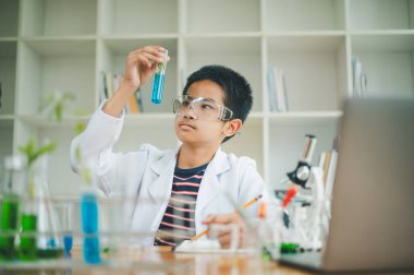 Asyalı erkek bilim öğrencileri mikroskopla bakıyorlar ve sınıfta bitki testleri yapıyorlar. Bitki türleri üzerinde bilimsel deneyler öğrenmek.