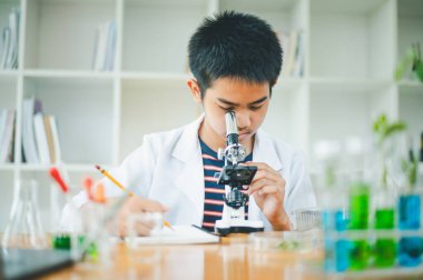 Asyalı erkek bilim öğrencileri mikroskopla bakıyorlar ve sınıfta bitki testleri yapıyorlar. Bitki türleri üzerinde bilimsel deneyler öğrenmek.