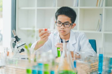 Asyalı erkek bilim öğrencileri mikroskopla bakıyorlar ve sınıfta bitki testleri yapıyorlar. Bitki türleri üzerinde bilimsel deneyler öğrenmek.